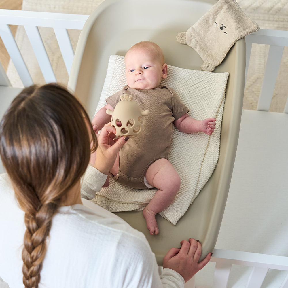 beige baby changing pad on top of cotbed