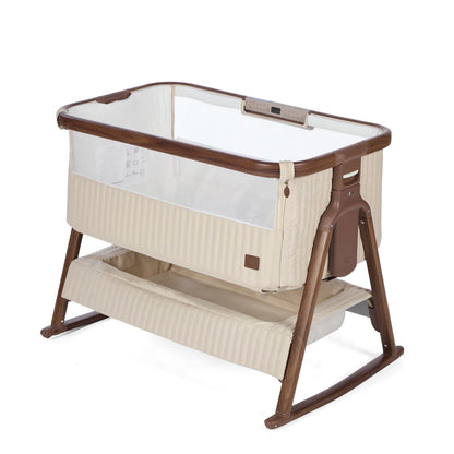 A portable baby bassinet with a cream-colored ribbed fabric body, clear mesh sides, and a dark brown wooden frame and rocking base, shown on a white background.