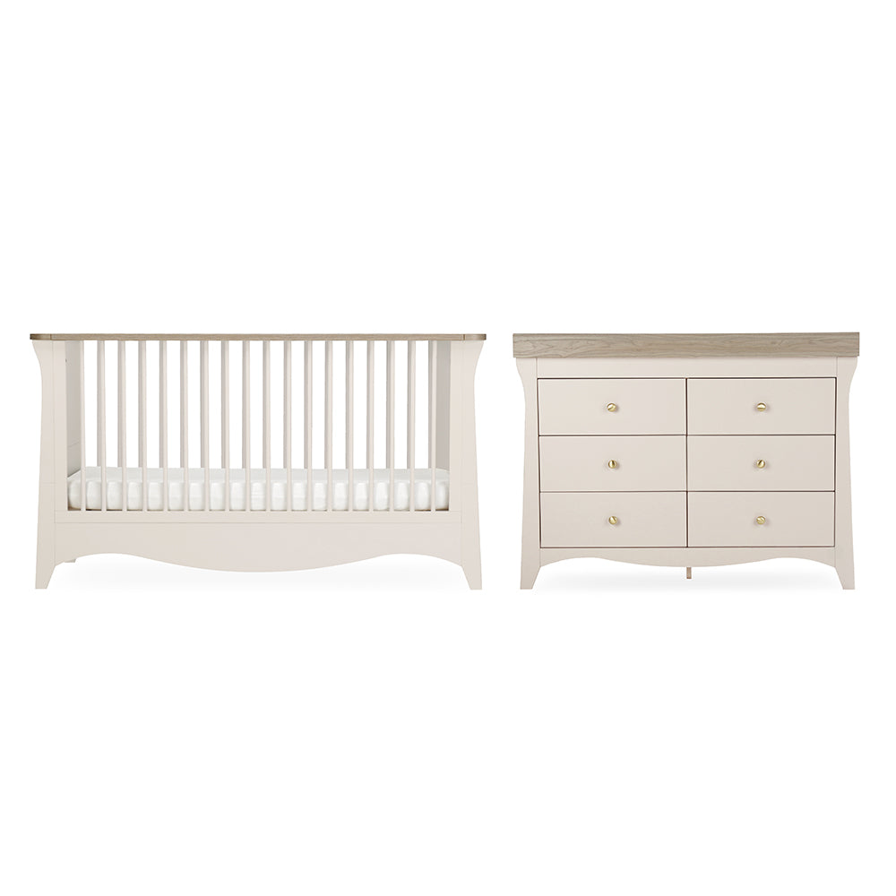 A baby nursery furniture set featuring a convertible crib and a six-drawer dresser in a warm off-white finish with light natural wood tops and small gold knobs, shown against a plain white background.