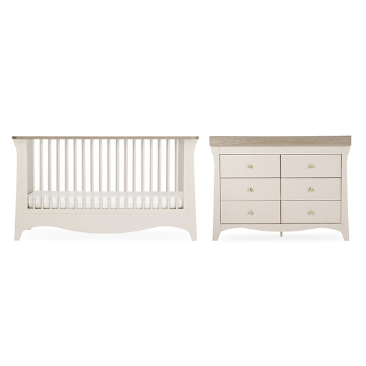 A baby nursery furniture set featuring a convertible crib and a six-drawer dresser in a warm off-white finish with light natural wood tops and small gold knobs, shown against a plain white background.