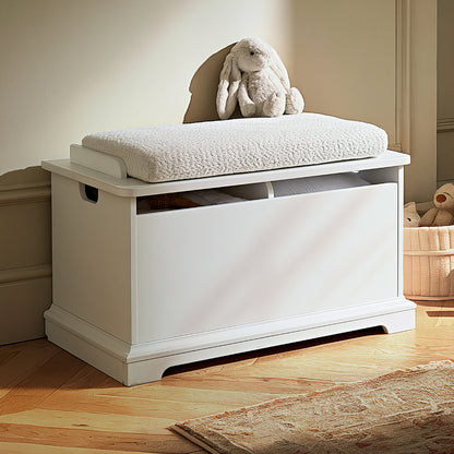 A white wooden toy storage bench with a cushioned seat, styled in a child's room with a plush bunny toy on top, a wooden floor, and a rug nearby.
